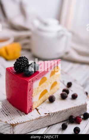 Une tranche de cheesecake rose à la fraise servie avec des baies fraîches sur un tableau blanc Banque D'Images