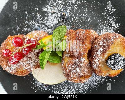 Beignets de pommes sur une assiette foncée avec du sucre et des fruits Banque D'Images