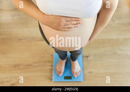 Photo recadrée en grand angle d'une femme enceinte se pesant sur une balance à la maison Banque D'Images