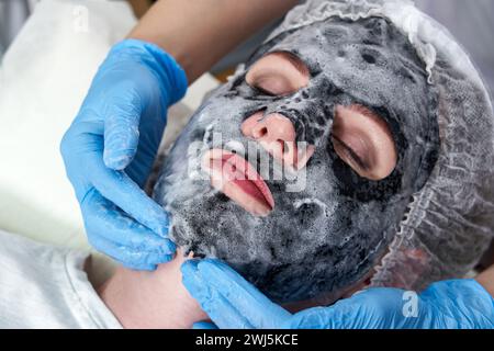 Jeune femme avec un masque à bulles d'oxygène noir sur son visage dans un salon de beauté Banque D'Images