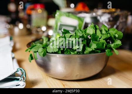 Un bol en acier inoxydable rempli de feuilles de coriandre vert vif, prêt à être utilisé comme herbe fraîche dans les recettes culinaires. Banque D'Images