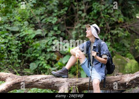 Jeune homme voyageur assis sur un arbre tombé et regardant la boussole à la main. Banque D'Images