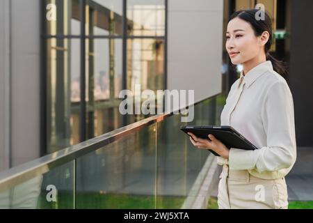 Une jeune femme asiatique sur un balcon avec une tablette, générée par IA. Banque D'Images