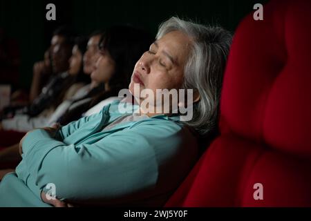 Femme senior s'endort en regardant un film au cinéma et pop-corn à la main, film manquant d'intéressant et ennuyeux. Banque D'Images