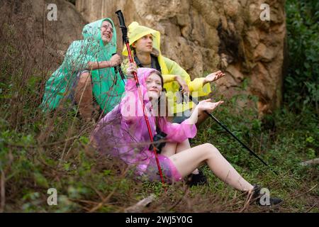 Groupe d'amis en imperméable avec sacs à dos randonnée dans la forêt, assis et abrité de la pluie Banque D'Images