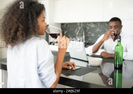 Les deux jeunes entreprises boivent du vin et utilisent leurs ordinateurs portables pour partager des informations les uns avec les autres dans leur salon de la maison. Banque D'Images