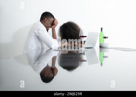 Les deux jeunes entreprises boivent du vin et utilisent leurs ordinateurs portables pour partager des informations les uns avec les autres dans leur salon de la maison. Banque D'Images