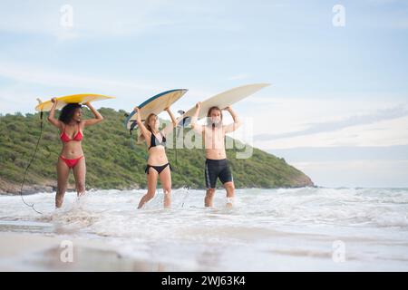 Vue arrière de deux femmes et d'un jeune homme tenant des planches de surf sur leur tête. et marcher dans la mer pour surfer Banque D'Images