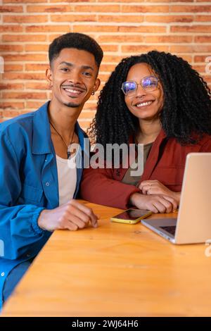 Portrait vertical heureux homme multiethnique et femme ont plaisir à naviguer sur Internet sur ordinateur portable à l'intérieur. Banque D'Images