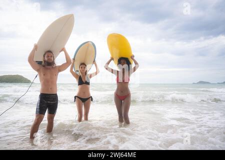 Vue arrière de deux femmes et jeune homme tenant des planches de surf sur leurs têtes et marchant dans la mer pour surfer Banque D'Images