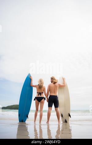 Vue arrière de jeune homme et femme en maillots de bain avec planches de surf sur la plage. Banque D'Images