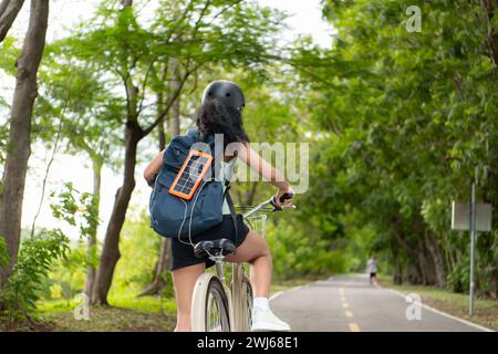 Vue arrière d'une femme asiatique chevauchant un vélo dans le parc. Il dispose d'un sac à dos avec un panneau solaire pour charger smartphone. Banque D'Images