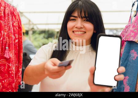 jeune femme vénézuélienne latine, touriste à la foire artisanale plaza italia à buenos aires, montrant l'écran de téléphone et la carte après avoir payé avec l'application de téléphone, technolog Banque D'Images