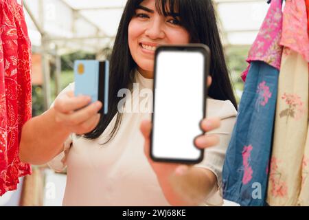 jeune femme vénézuélienne latine, touriste à la foire artisanale plaza italia à buenos aires, montrant l'écran de téléphone et la carte après avoir payé avec l'application de téléphone, technolog Banque D'Images