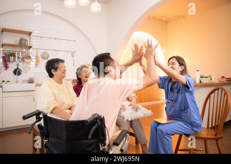 Groupe de personnes âgées et homme senior en fauteuil roulant avec infirmière à la maison de soins infirmiers jouer un jeu amusant de frapper les mains de l'autre. Personnes âgées Banque D'Images