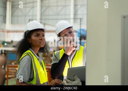 Portrait de deux ingénieurs féminins utilisant un ordinateur portable tout en se tenant debout en usine, pour vérifier le fonctionnement de la carte de circuit imprimé de la machine. Banque D'Images