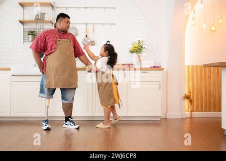 Une famille de grande taille avec un père portant une jambe prothétique, la fille s'est amusée à jouer avec son père avant d'aider à cuisiner. po Banque D'Images