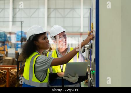 Portrait de deux ingénieurs féminins utilisant un ordinateur portable tout en se tenant debout en usine, pour vérifier le fonctionnement de la carte de circuit imprimé de la machine. Banque D'Images