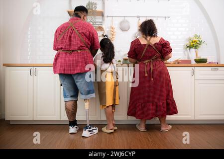 Une grande famille avec un père portant une jambe prothétique, ils font le petit déjeuner ensemble avec plaisir dans la salle de cuisine de th Banque D'Images