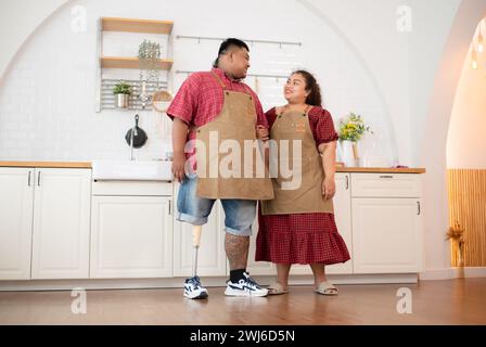 Un couple familial de grande taille avec un père portant une jambe prothétique se prépare à cuisiner dans la salle de cuisine de la maison Banque D'Images