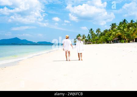 Un couple d'hommes et de femmes avec des chapeaux d'été marchant à la plage de Koh Muk Banque D'Images