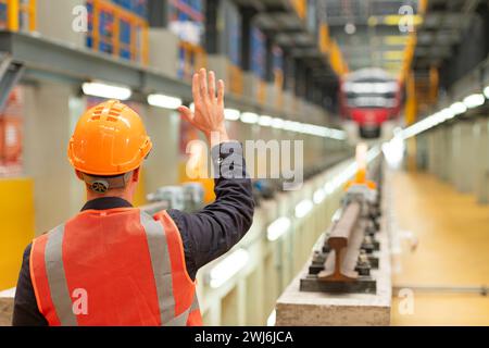 Vue arrière de l'ingénieur de l'industrie du train électrique portant un casque de sécurité et un gilet réfléchissant. Il y a une voiture électrique dans la voiture R. Banque D'Images