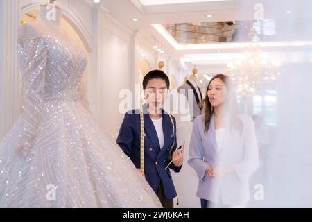 Les deux créateurs de mode asiatiques travaillant avec robe de mariée dans la boutique de robe de mariée Banque D'Images