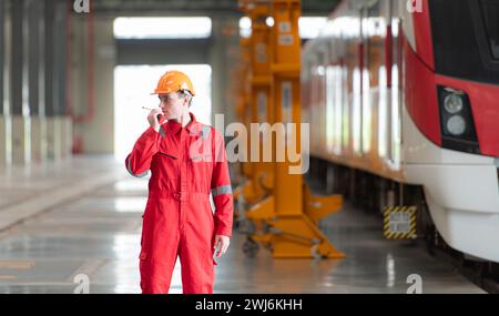Portrait d'un technicien utilisant un talkie-walkie devant un train pour communiquer avec ses collègues après avoir inspecté l'élec Banque D'Images