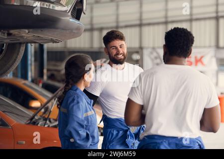 Portrait de l'équipe souriante de mécaniciens dans l'atelier de réparation automobile, parlant les uns les autres tout en se tenant devant la voiture Banque D'Images