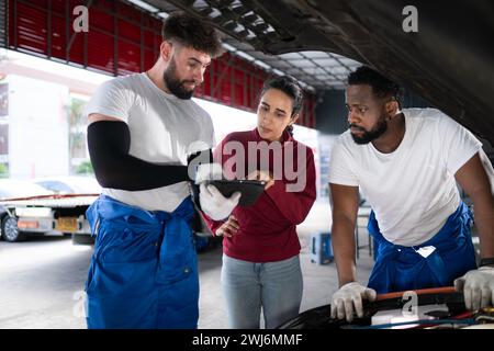 Dans un atelier de réparation automobile, Un homme mécanicien automobile professionnel informe une cliente sur le coût des réparations de voiture et perçoit le salaire Banque D'Images