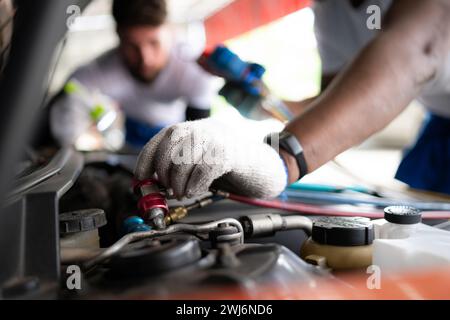 Mécanicien automobile travaillant dans un atelier de réparation automobile, inspectant le fonctionnement du climatiseur et du réfrigérant de la voiture. Banque D'Images