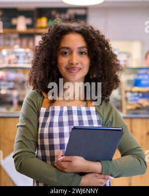 Portrait d'une jeune femme portant tablier travaillant dans un magasin d'alimentation à l'aide d'une tablette numérique Banque D'Images
