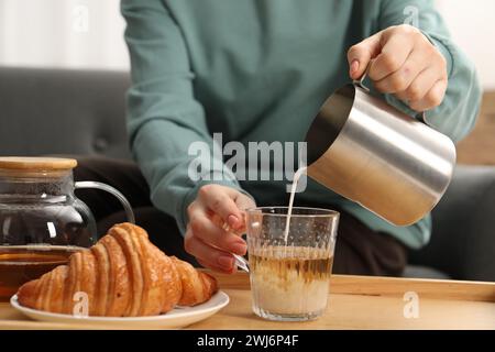 Femme versant du lait dans la tasse avec du thé aromatique à la table à l'intérieur, gros plan Banque D'Images