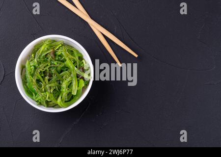 Salade d'algues Chuka dans une assiette avec des baguettes sur un fond sombre Banque D'Images