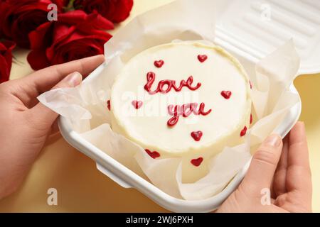 Femme tenant une boîte à emporter avec bento cake à la table beige, gros plan. Prog Surprise pour la Saint-Valentin Banque D'Images