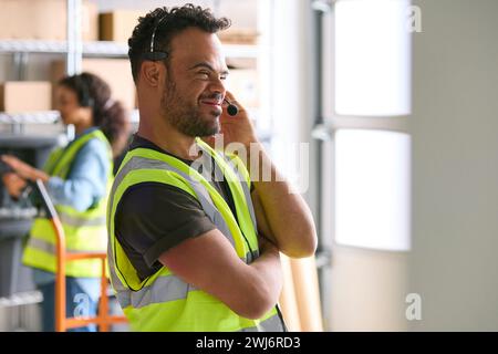 Homme atteint du syndrome de Down travaillant dans un entrepôt portant un casque Banque D'Images