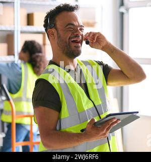 Homme atteint du syndrome de Down travaillant dans un entrepôt portant un casque à l'aide d'une tablette numérique Banque D'Images