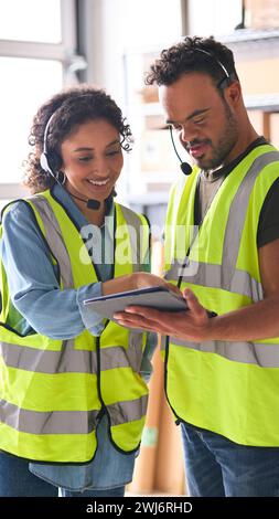 Femme utilisant la tablette numérique et collègue masculin avec le syndrome de Down dans l'entrepôt portant des casques Banque D'Images