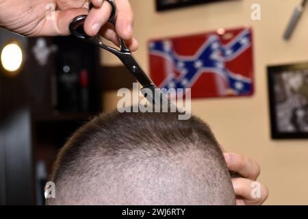 La photo montre un homme se faisant couper les cheveux dans un salon. Un coiffeur utilise des ciseaux pour enlever les cheveux de la tête d'un client. Banque D'Images