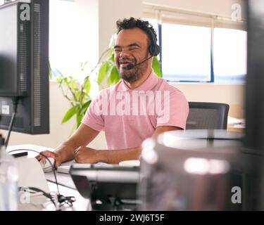 Homme atteint du syndrome de Down portant un casque travaillant dans le centre d'appels du bureau Banque D'Images