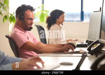 Homme atteint du syndrome de Down portant un micro-casque travaillant dans l'équipe du centre d'appels du bureau Banque D'Images