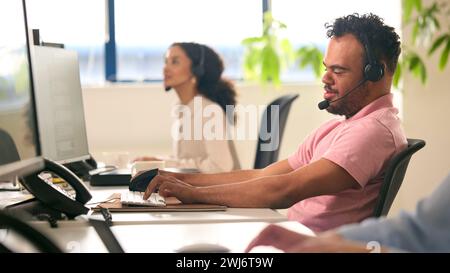 Homme atteint du syndrome de Down portant un micro-casque travaillant dans l'équipe du centre d'appels du bureau Banque D'Images