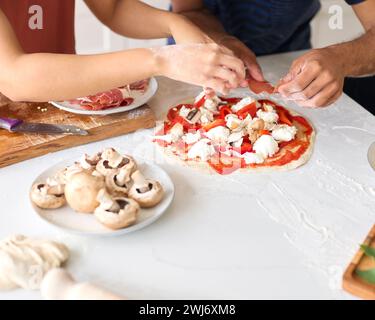 Gros plan de couple at Home Taking Toppings on Pizza in Kitchen Together Banque D'Images