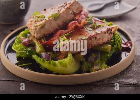 Steaks de thon poêlés avec bacon sur un lit de légumes. Banque D'Images