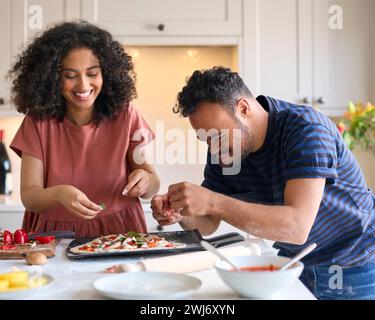Couple à la maison avec l'homme avec le syndrome de Down et femme mettant des garnitures sur Pizza dans la cuisine ensemble Banque D'Images