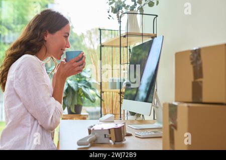 Femme buvant du café en cours d'exécution des affaires en ligne de la maison de travail à l'ordinateur Banque D'Images