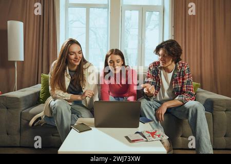 Discussion en direct. Jeunes, hommes et femmes, amis assis sur le canapé à la maison et réservation de voyage en ligne via ordinateur portable. Choisir les transports et les hôtels Banque D'Images