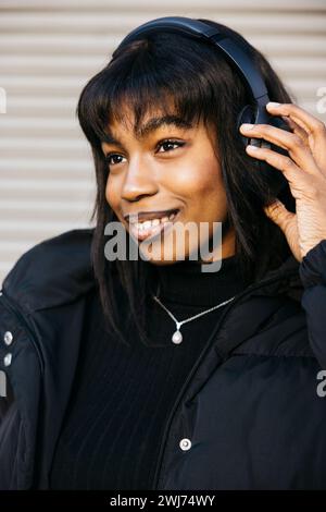 Portrait d'une jeune femme noire avec des écouteurs sans fil dansant à l'extérieur. Banque D'Images