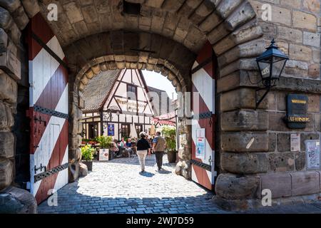 Les touristes seniors traversent la porte du Handwerkerhof à Nuremberg, en Allemagne, une cour d'artisans dans la vieille ville avec des boutiques d'artisanat et des restaurants. Banque D'Images