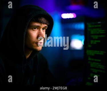 Photo d'un pirate informatique masculin assis devant des écrans violant la cybersécurité Banque D'Images